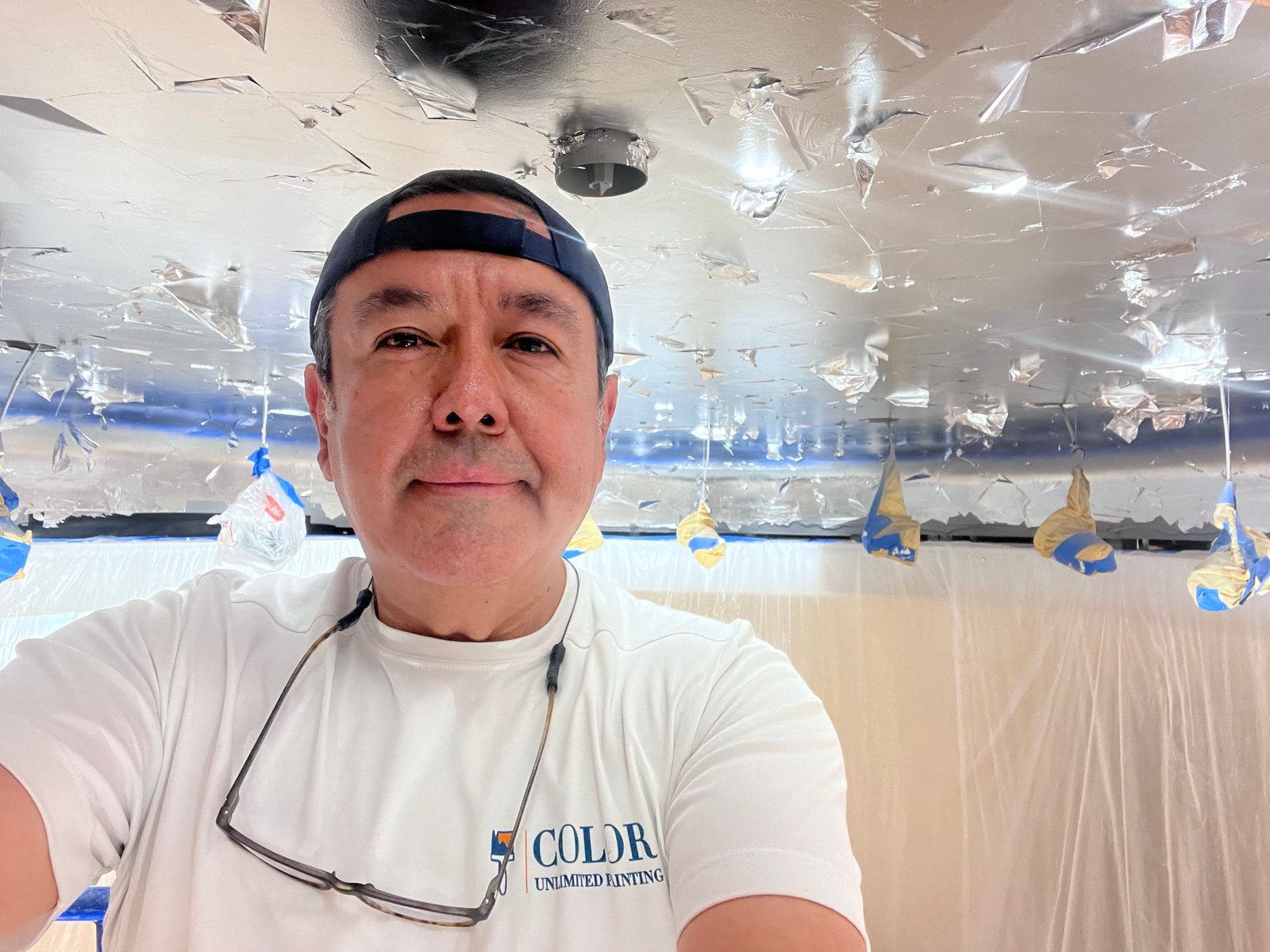 Alex in a Color Unlimited shirt beneath a leaf-covered ceiling with protected light fixtures during a commercial project.