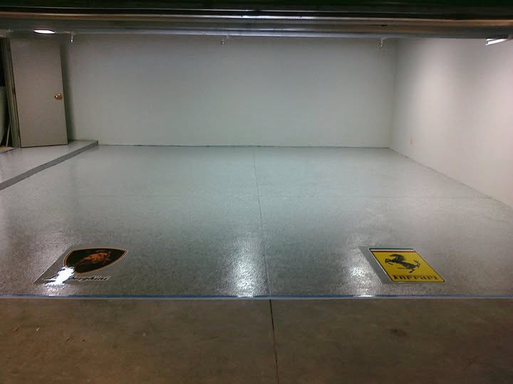 Wide view of a gray speckled epoxy floor with two automotive emblems near the front edge.