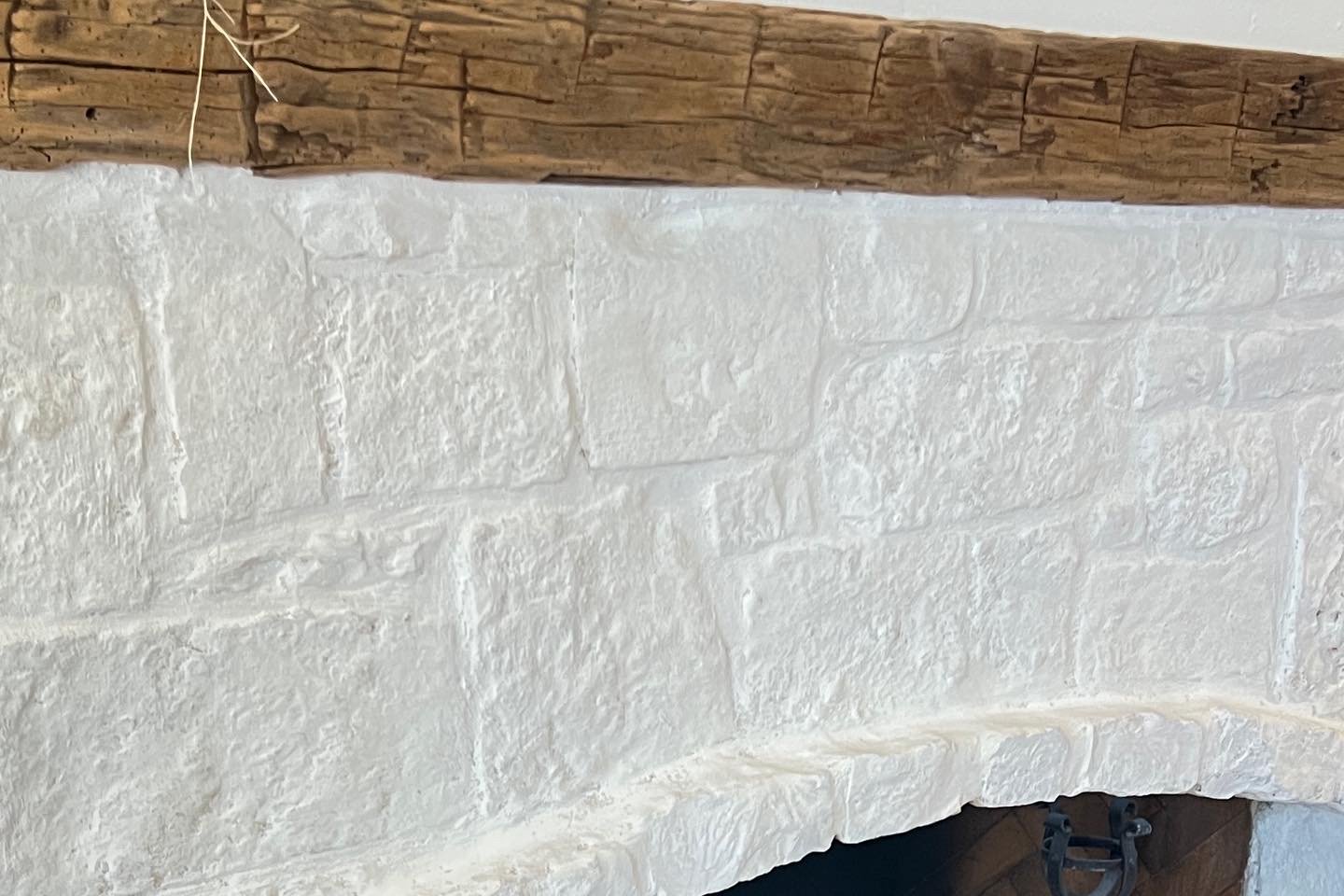 Finished pale limewash on textured stone beneath a rustic wood mantel, with the fireplace opening below.