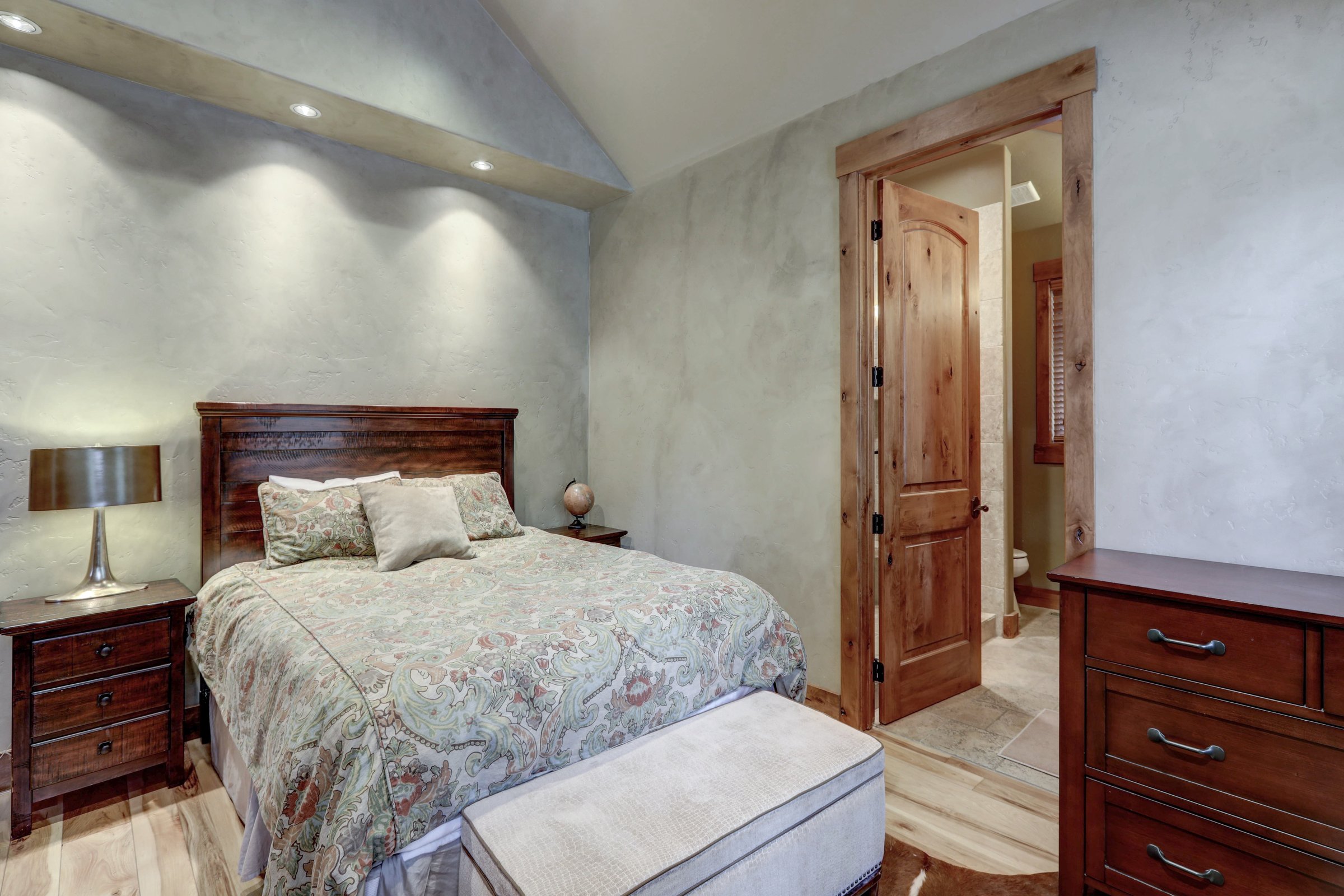 Bedroom with softly varied pale Venetian plaster walls, recessed lighting and warm wood furniture and trim.