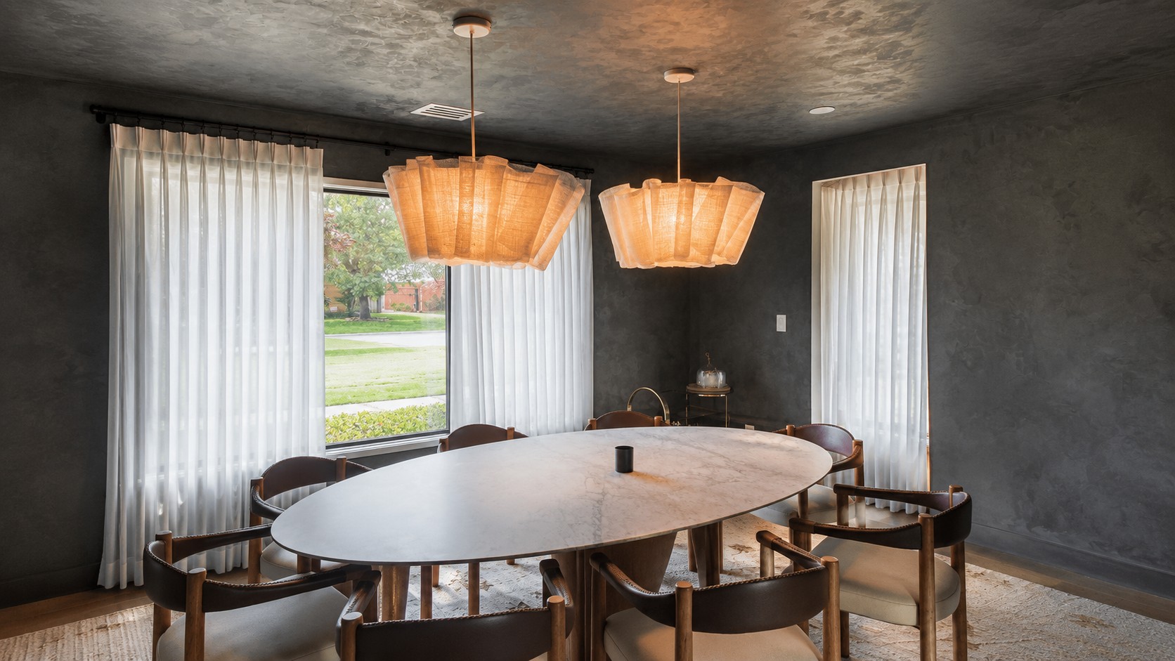 Finished charcoal decorative plaster dining room in University Park with an oval marble table and sculptural pendant lights