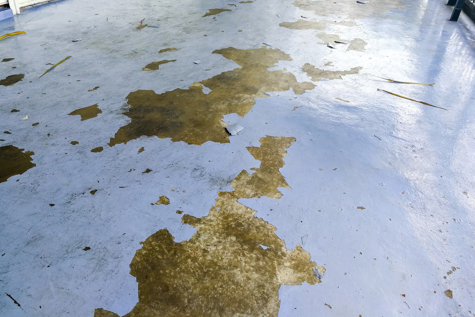 Wider view of an existing blue-gray floor coating with several peeling areas and exposed concrete.