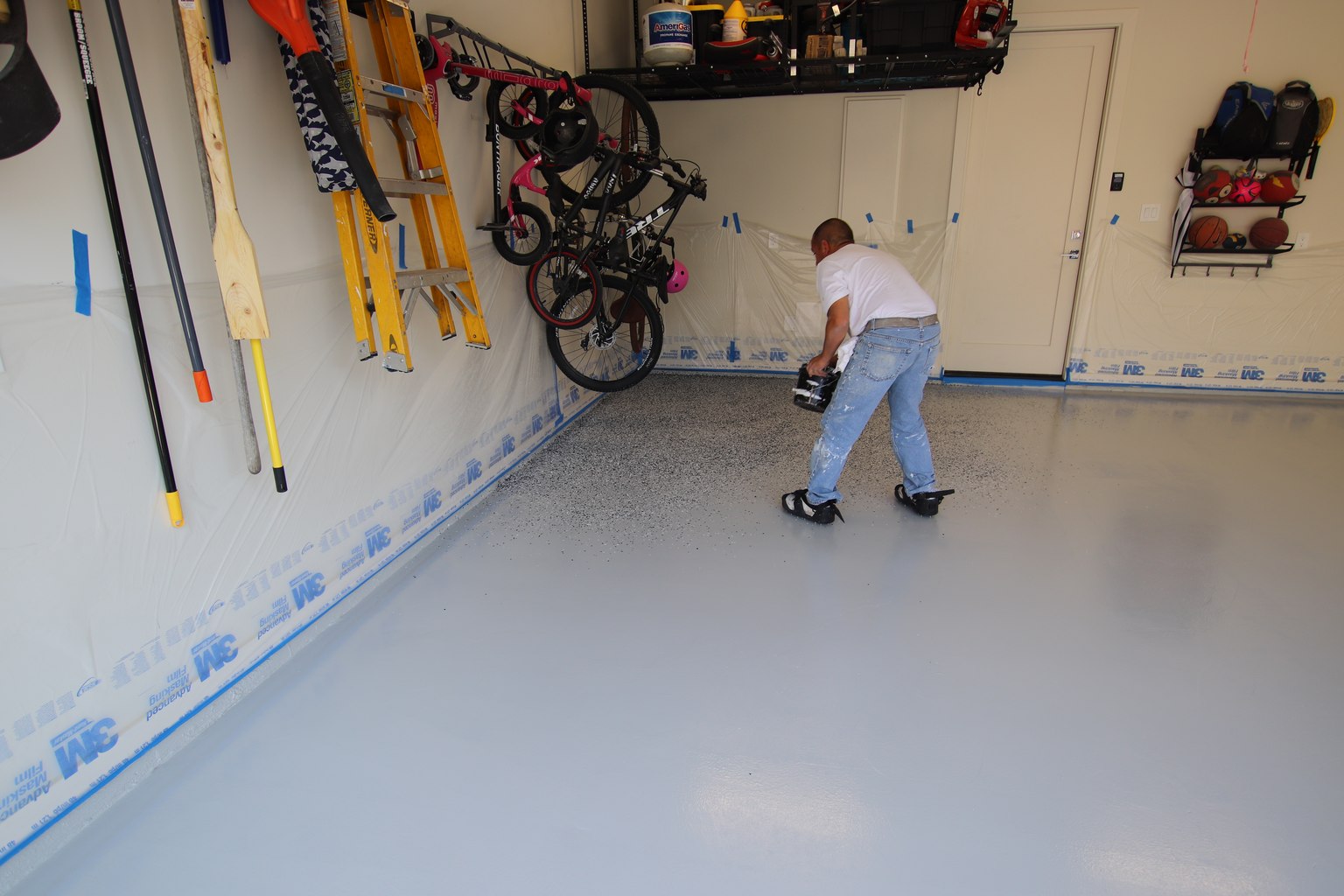 Worker scattering dark and light decorative flakes across a freshly coated gray garage floor.