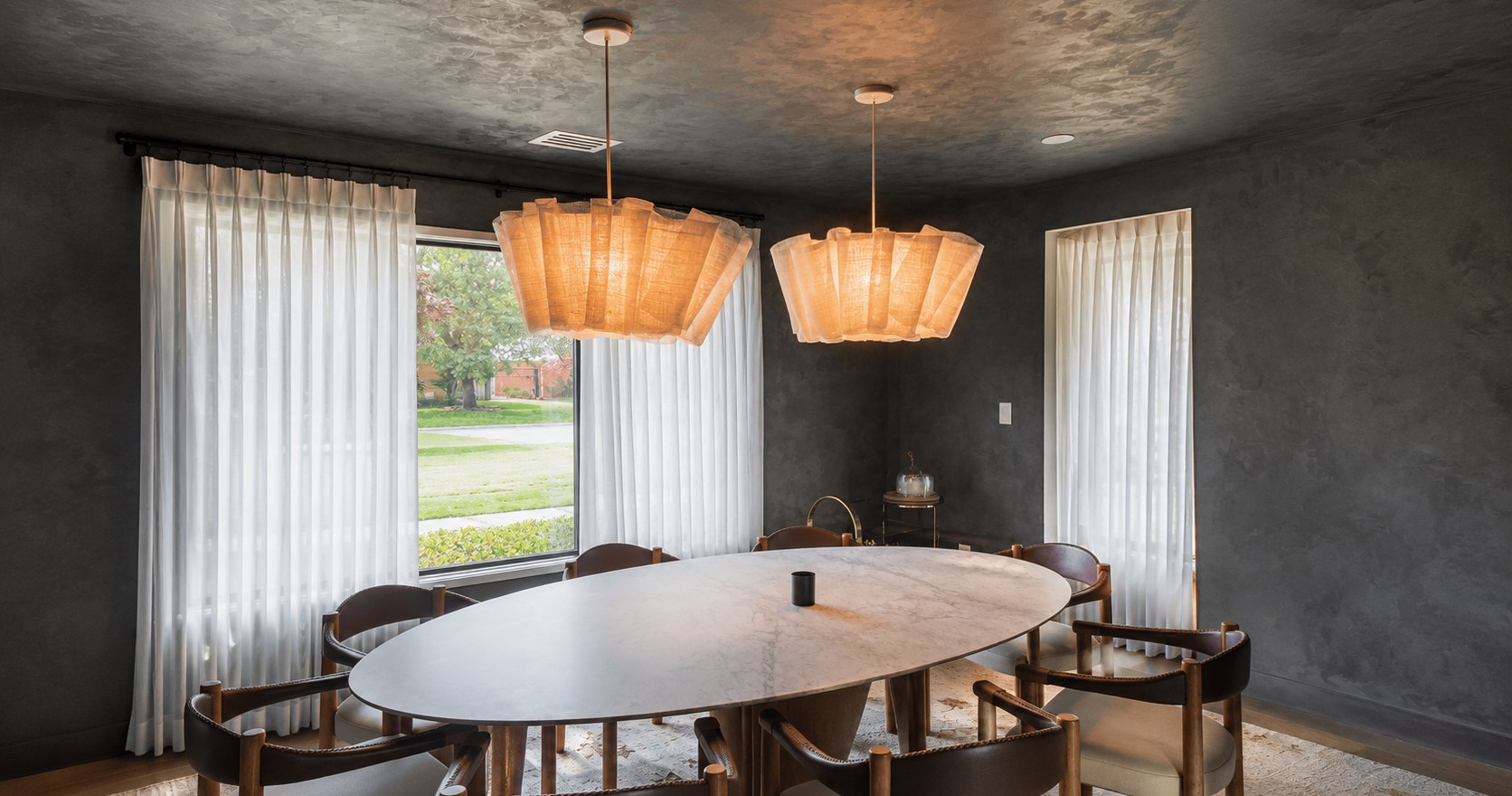 Dining room with charcoal textured walls and ceiling, sculptural pendant lights, a table and large windows.