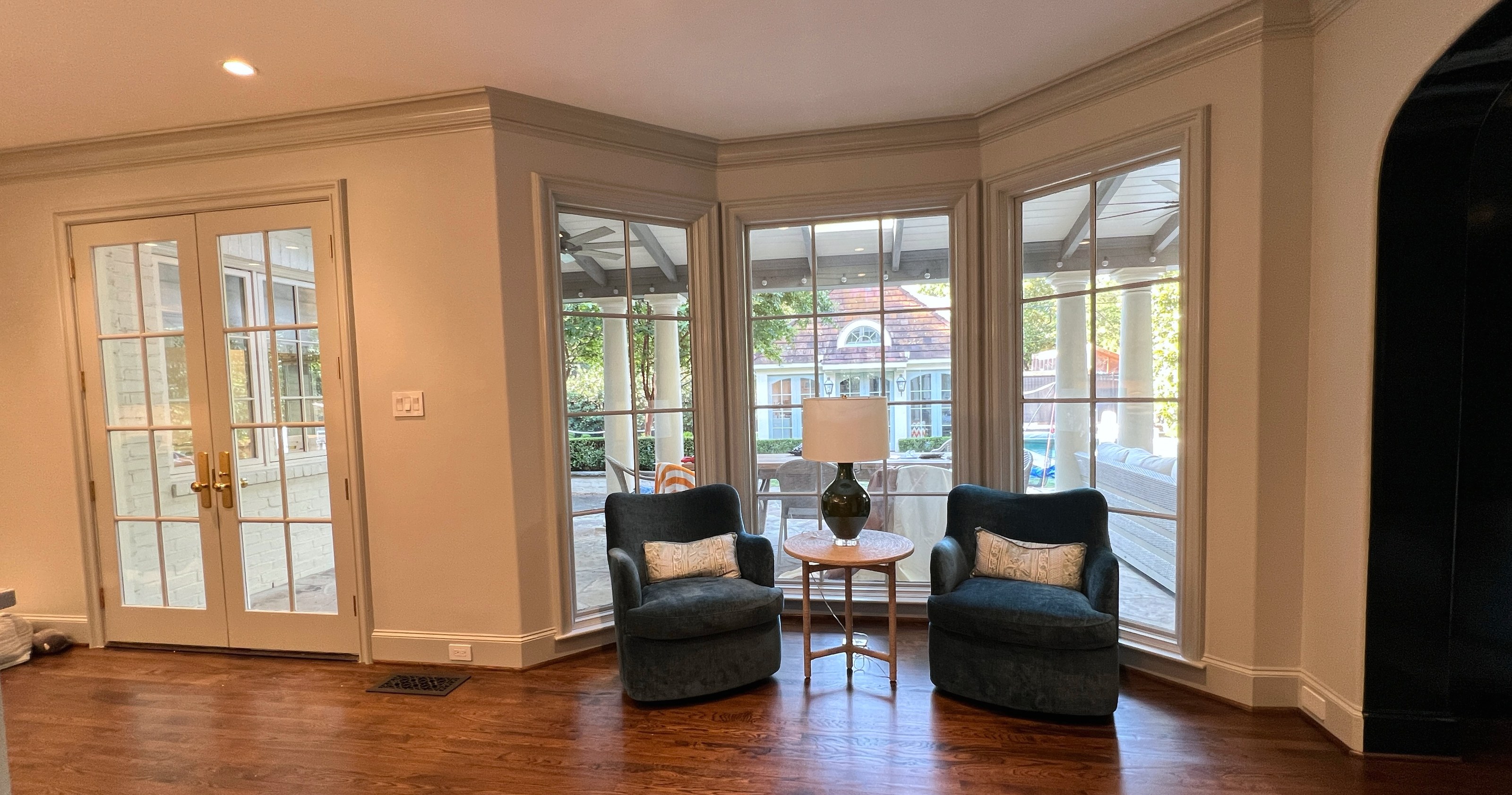 Bay window sitting area with pale walls and trim, French doors, two upholstered chairs, and wood floor.