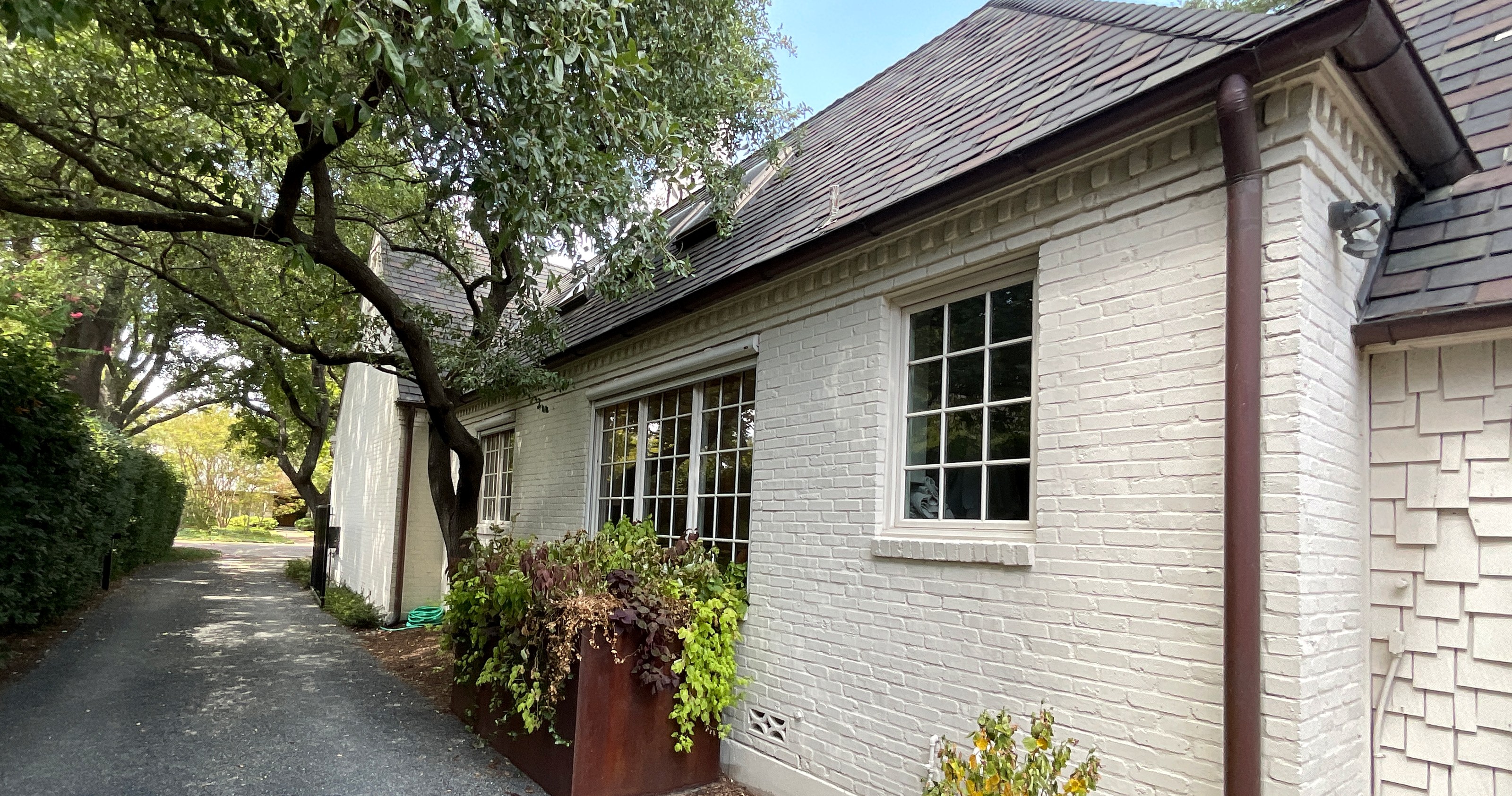 Painted brick home exterior with white window trim beside a tree lined driveway.