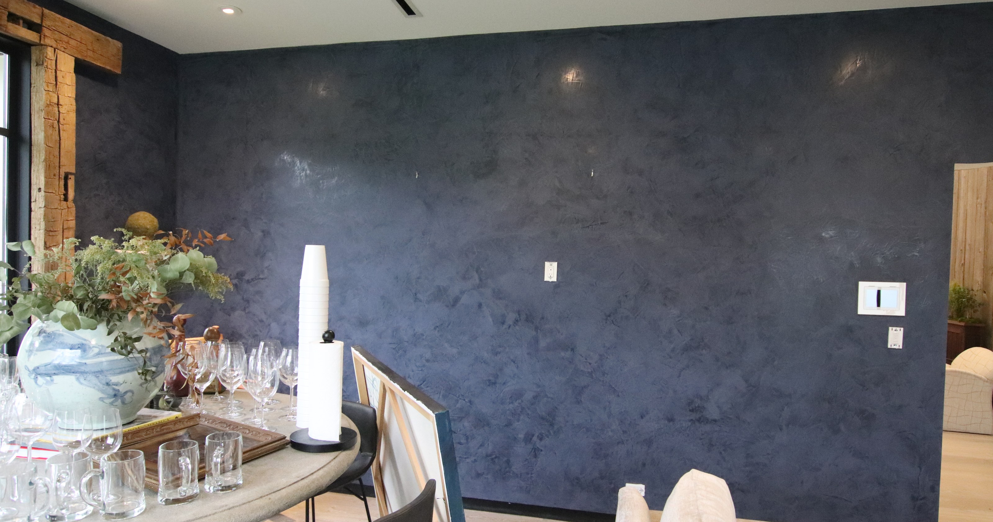 Dark textured feature wall in a furnished interior with a dining table in the foreground.