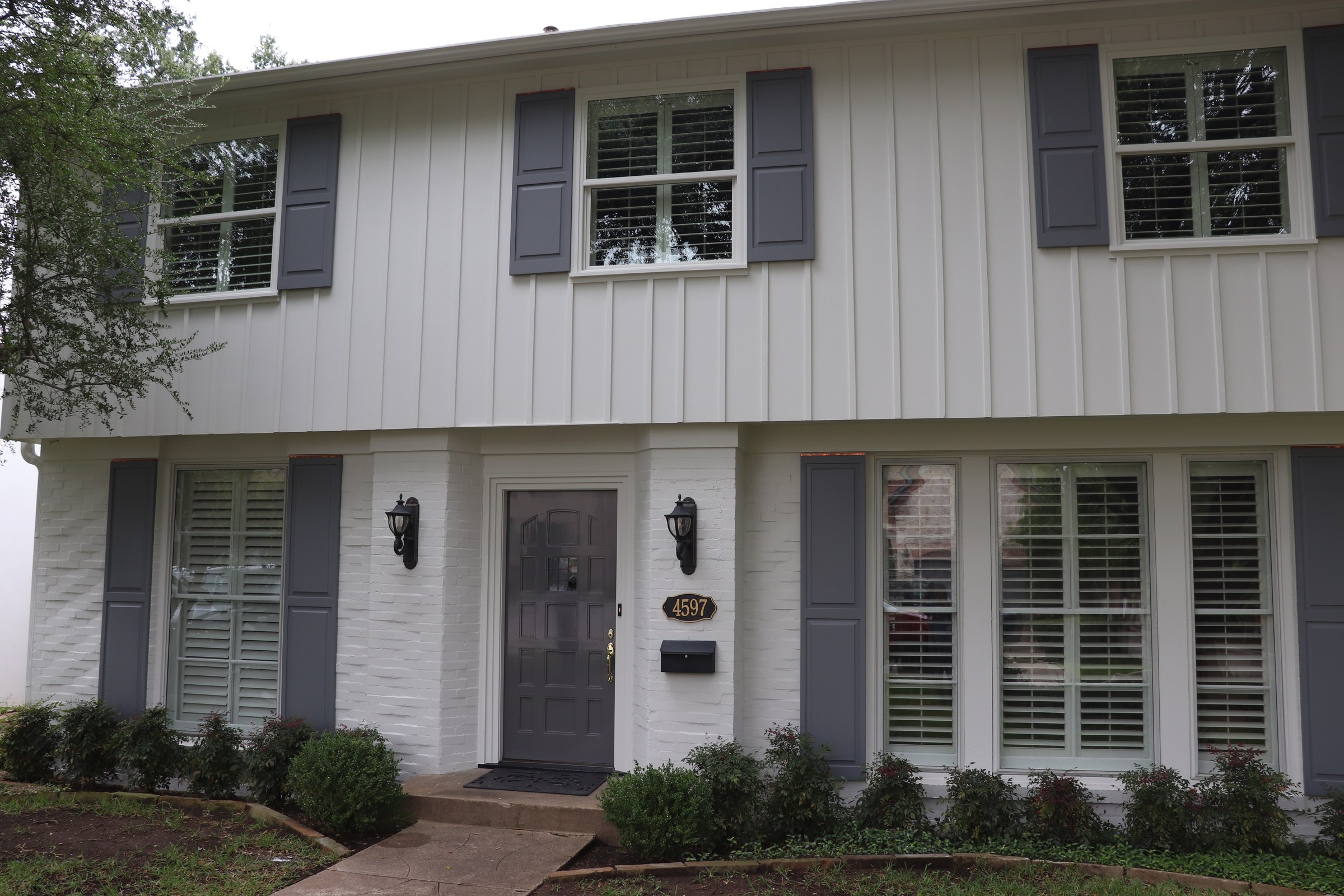 White painted house facade with vertical siding, window trim, brick, and dark shutters.