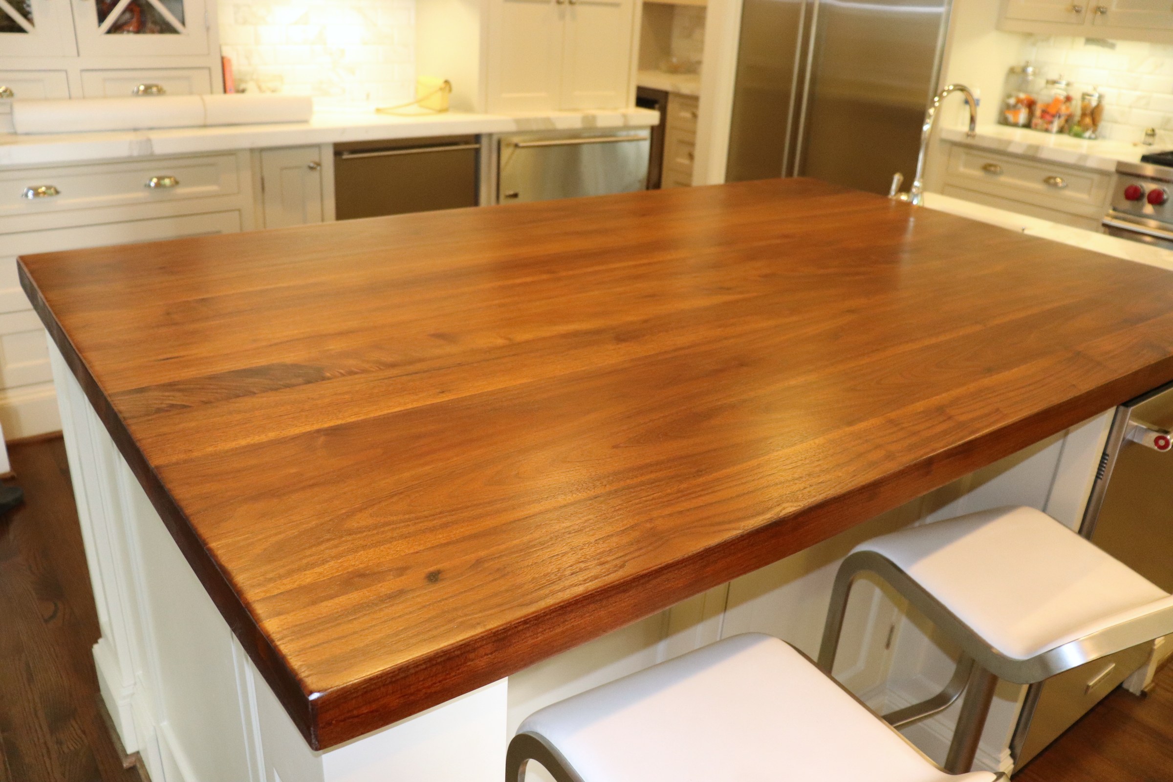 Warm wood-topped kitchen island with visible grain in a white kitchen.