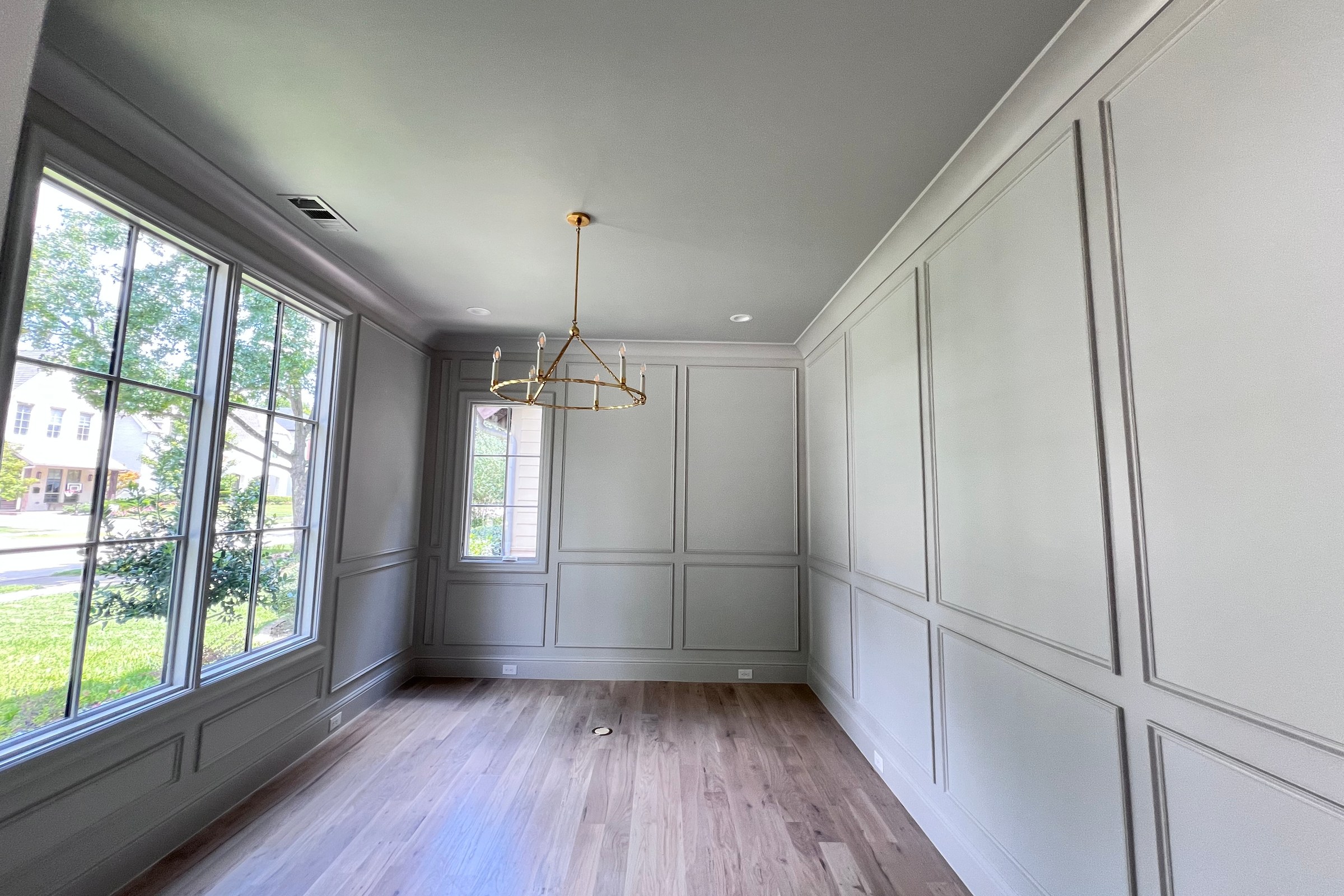 Finished interior room with pale paneled walls, white ceiling, wood floor, and tall windows.