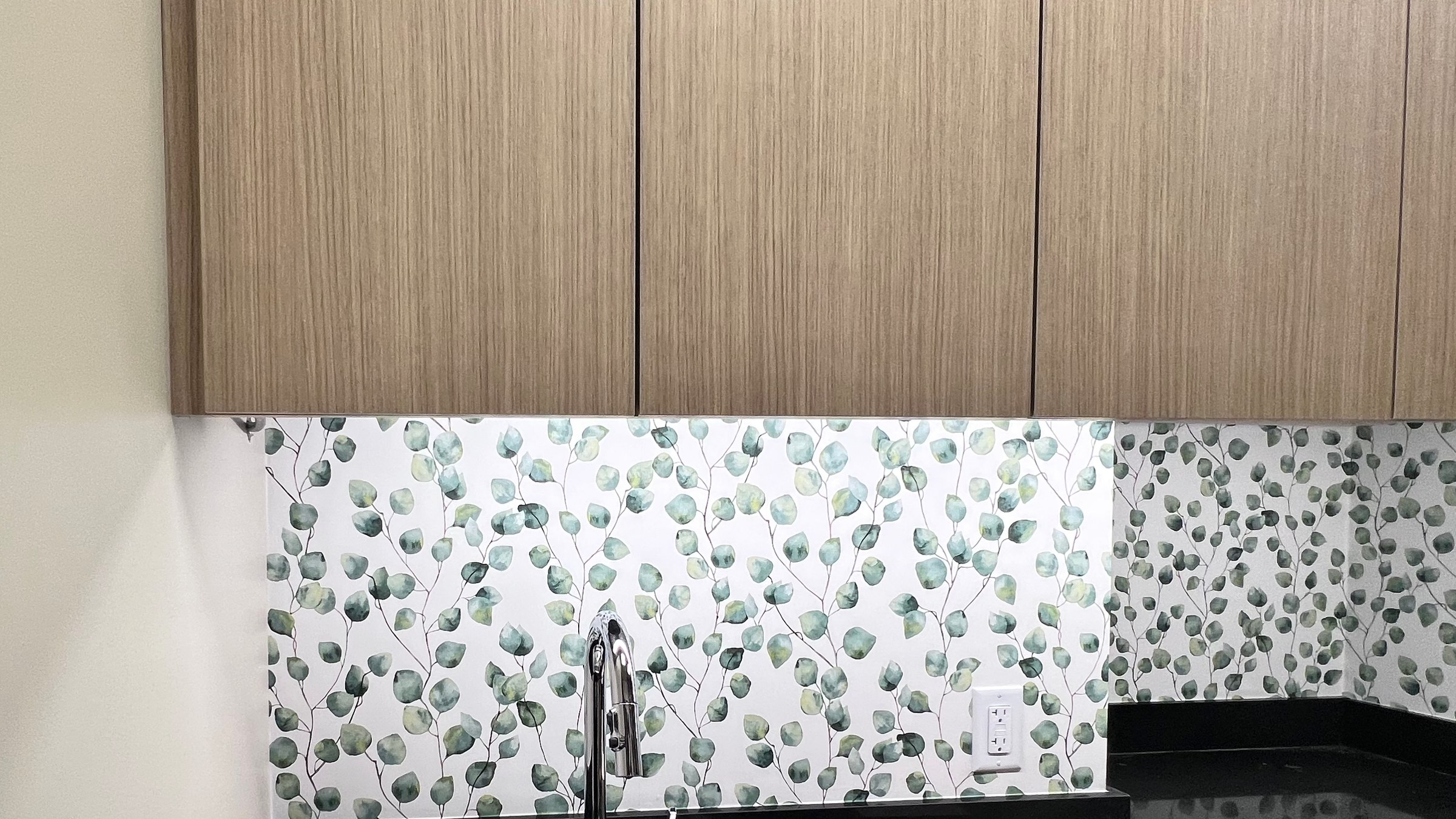 Botanical wallpaper installed around a sink and beneath wood-toned cabinetry.