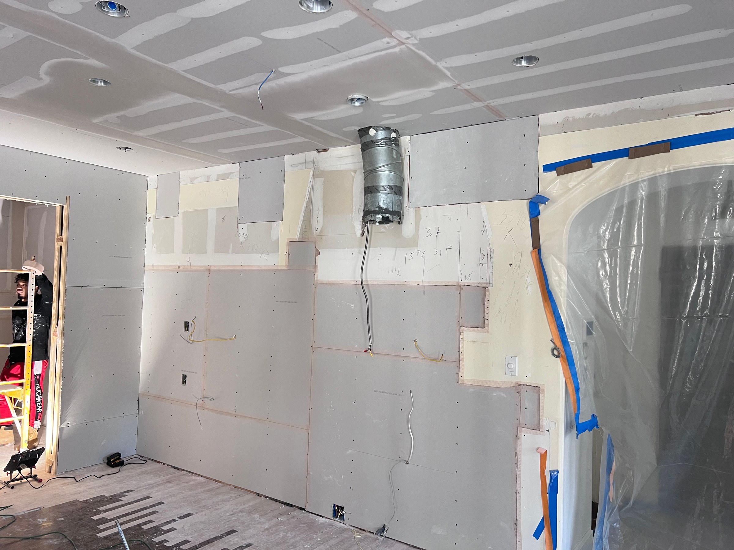 Room with newly installed drywall, taped ceiling seams, and protected opening before finishing.