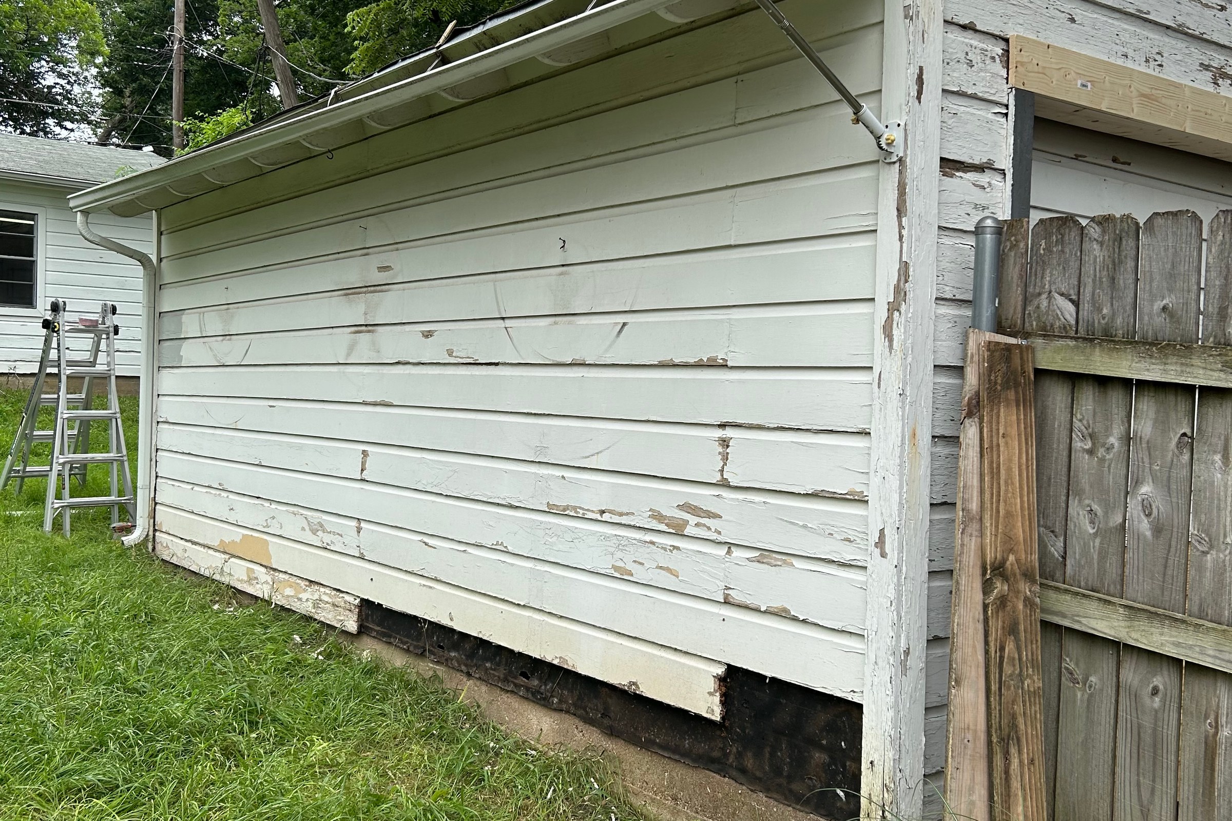 Peeling paint and damaged lower boards on white horizontal siding.