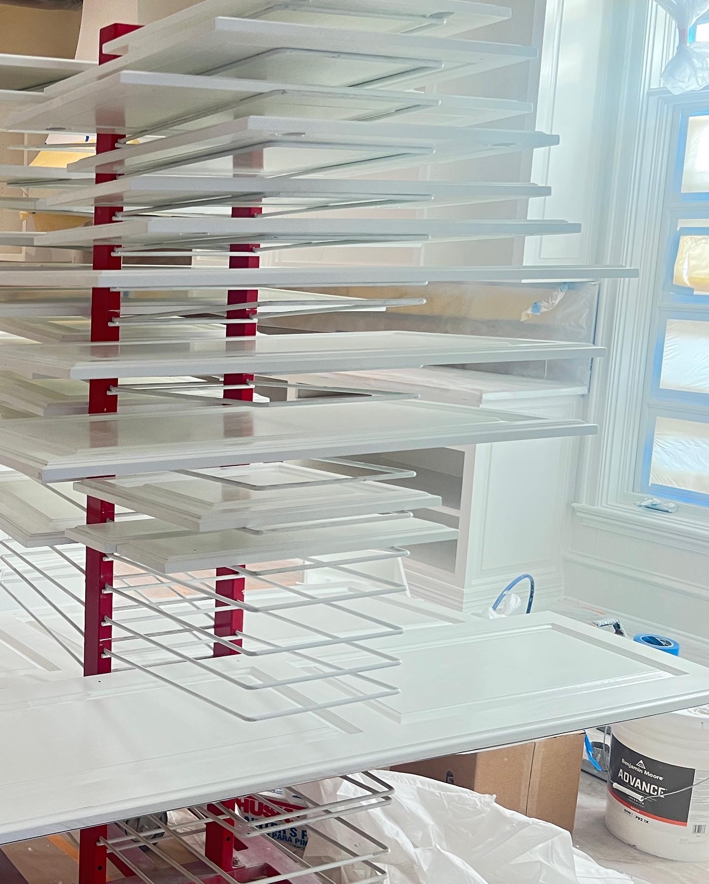 White cabinet doors rest separately on a red drying rack in a protected work area.