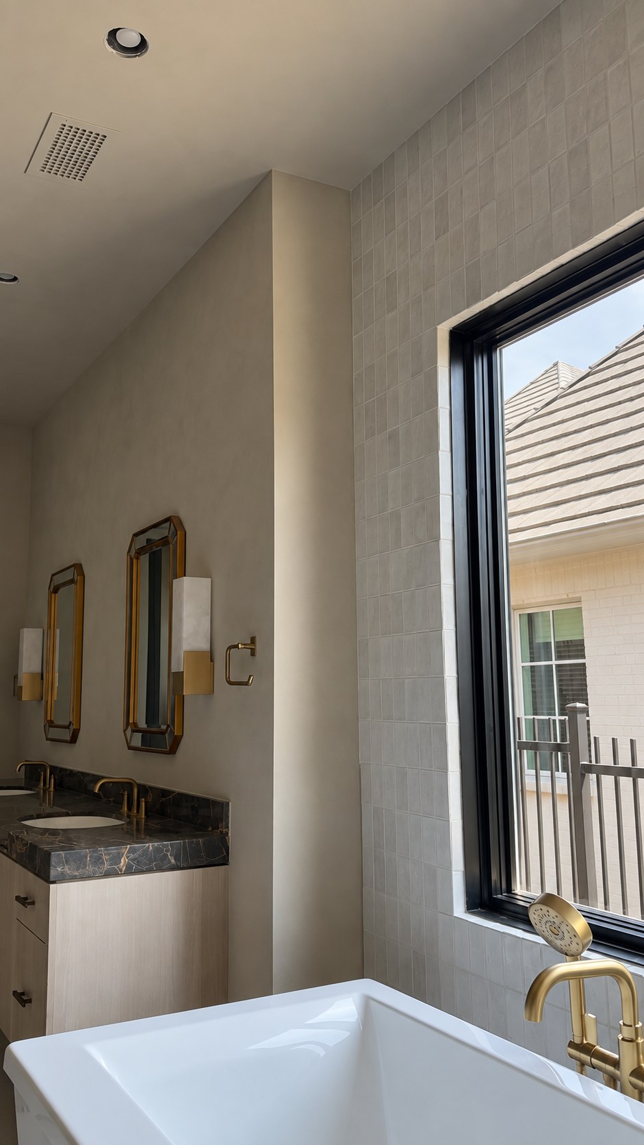 Interior limewash project with a dark stone vanity, brass fixtures and a white tub.