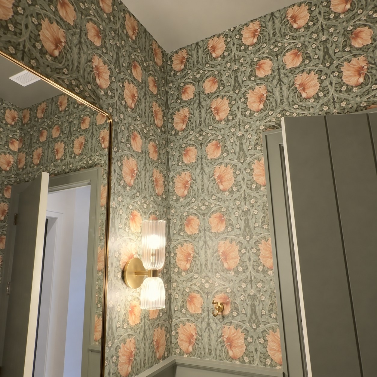 Floral wallpaper beside a mirror and brass wall sconce.